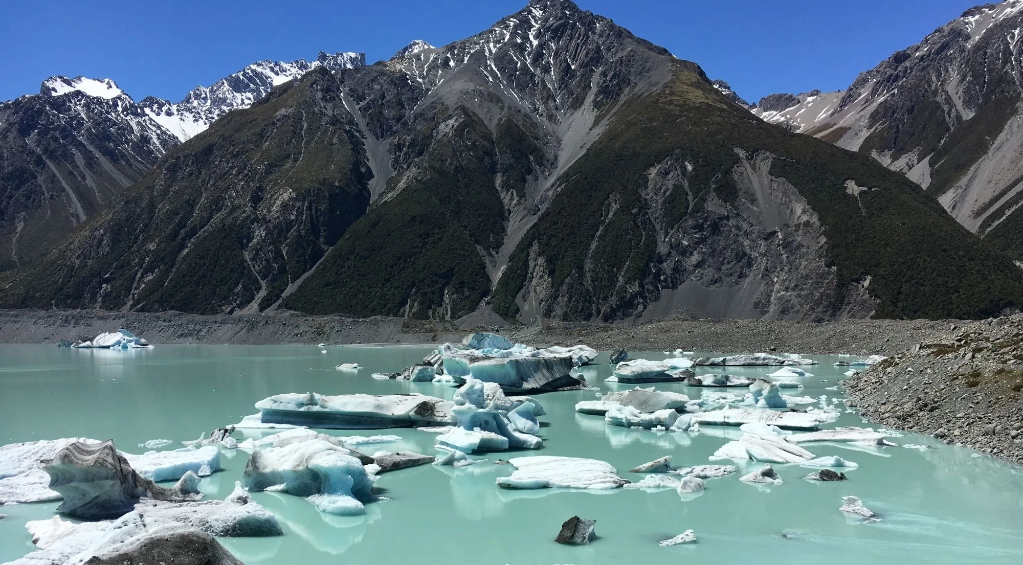 Icebergs floating on a milky glacier lake below dark mountain slopes