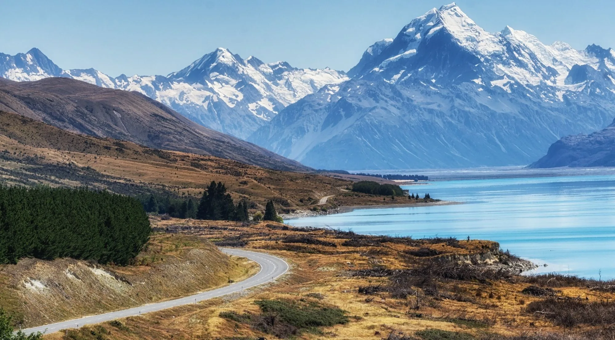 The road curving along the shore of Lake Pūkaki towards the Southern Alps