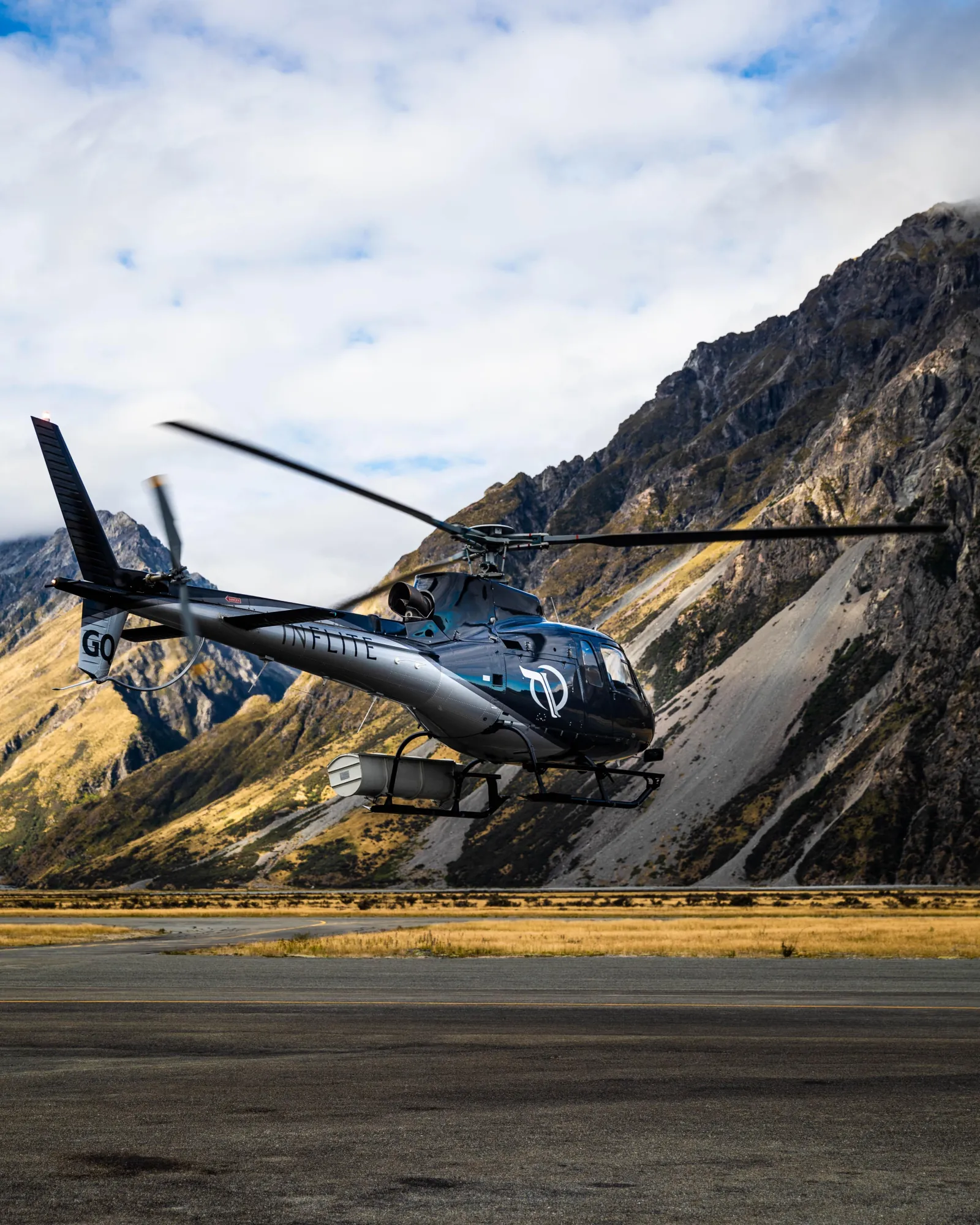INFLITE helicopter lifting off at Mount Cook Airport in front of a steep valley wall