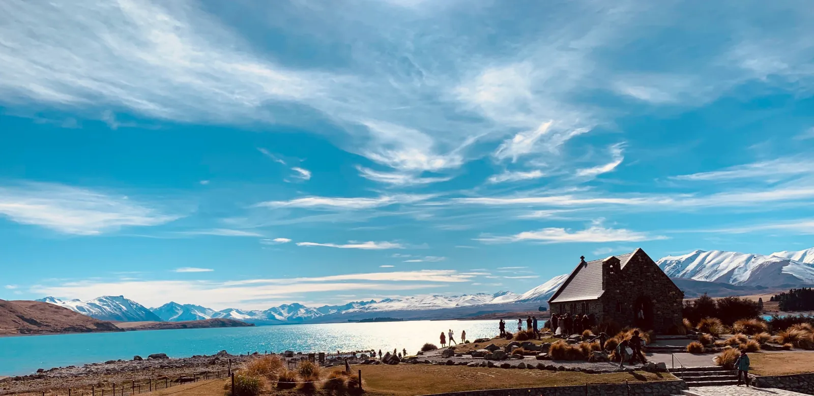 Visitors outside the Church of the Good Shepherd beside Lake Tekapo, with snow on the ranges across the water