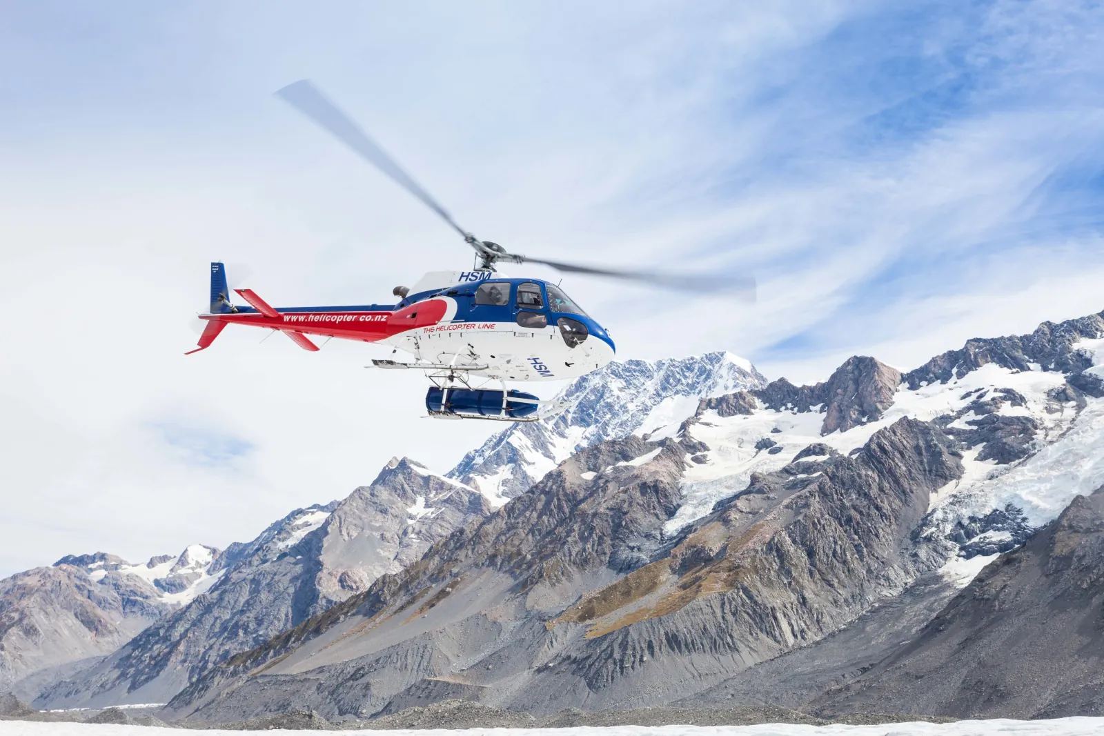 The Helicopter Line helicopter lifting off above the glacier ice with snowy Southern Alps peaks behind
