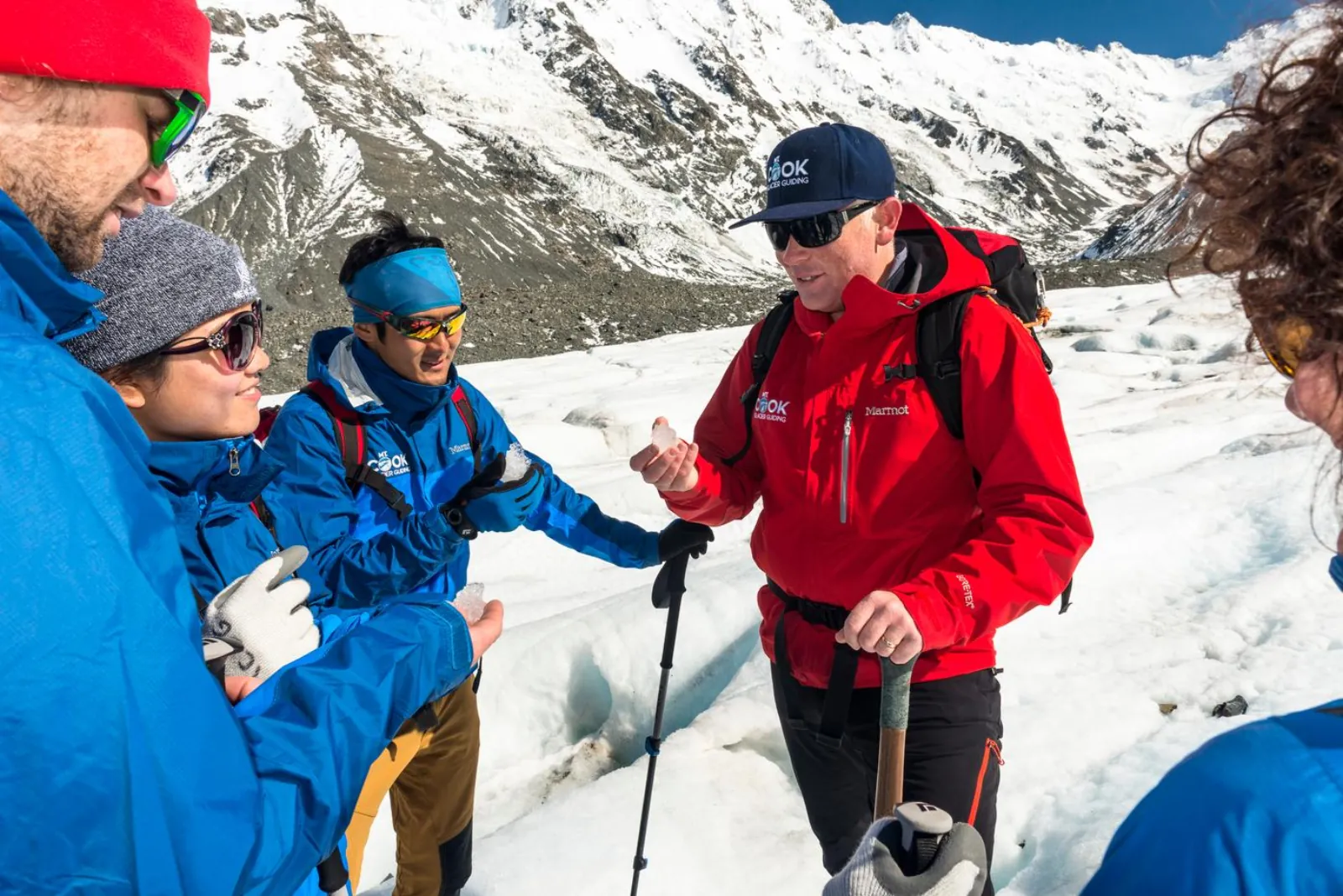Mt Cook Glacier Guiding guide showing hikers a piece of clear glacier ice beside a crevasse