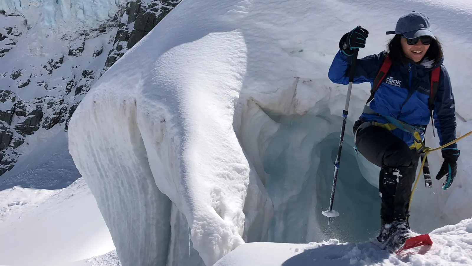 Hiker with a pole and snowshoes stepping past a blue ice crevasse on a guided glacier walk