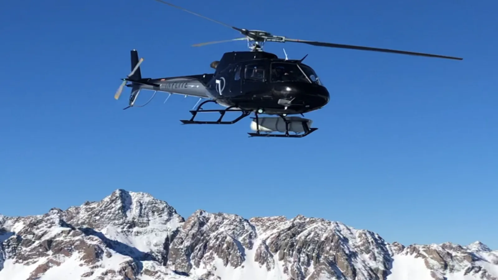 Black helicopter flying above snow-covered peaks of the Southern Alps