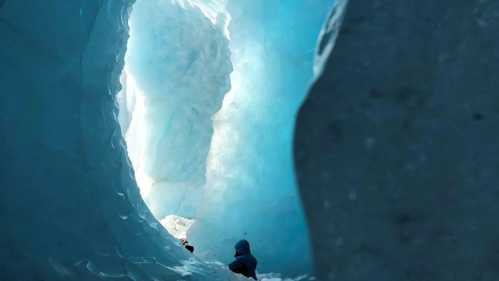 Hiker in a hooded jacket inside a blue ice cave on the glacier