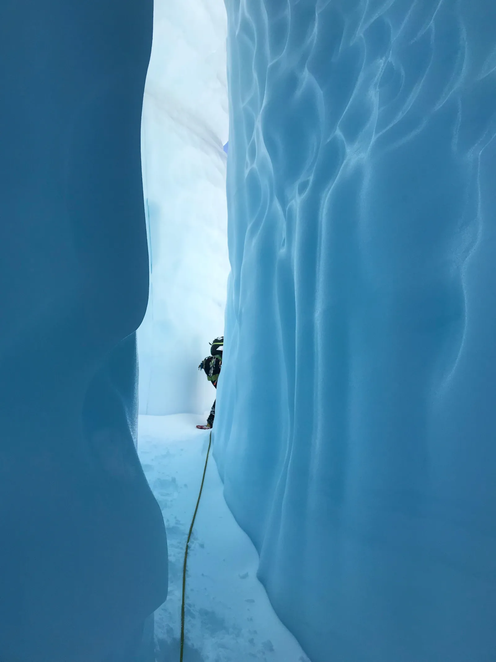 Roped glacier hiker at the end of a narrow corridor of blue ice