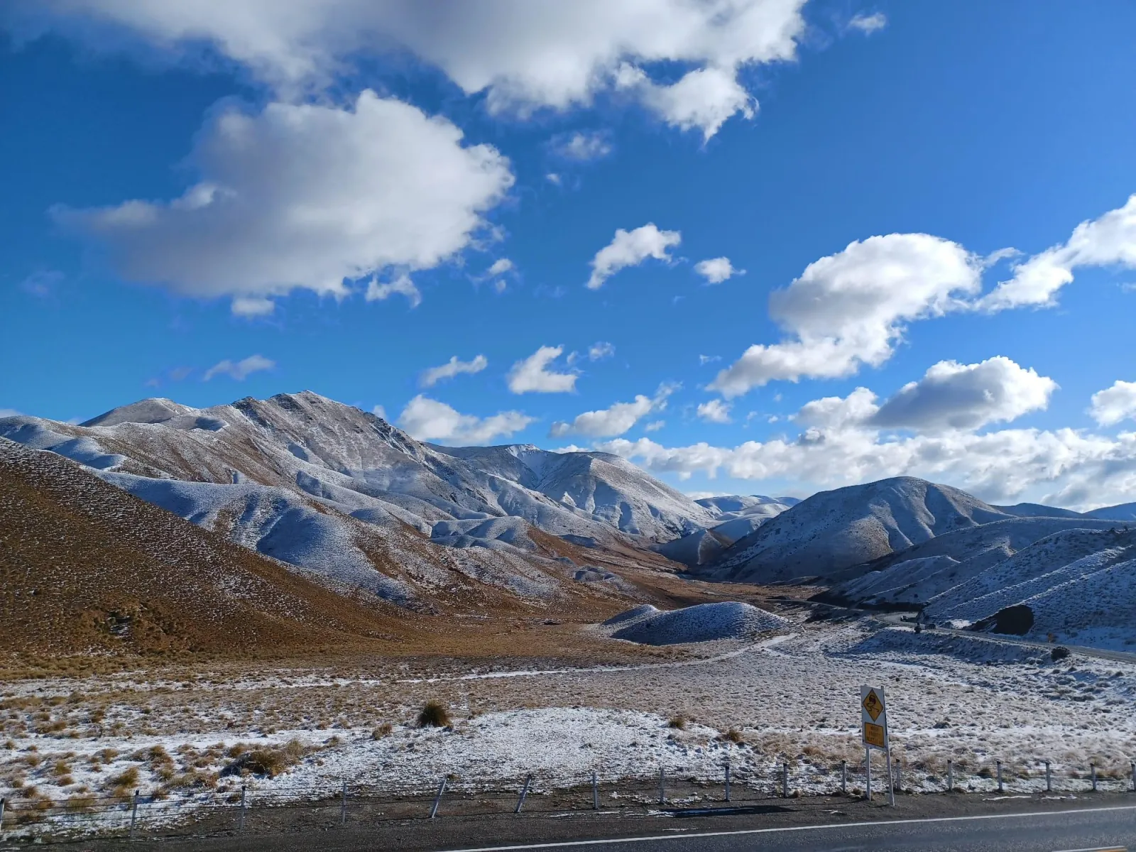 Snow-dusted tussock hills beside the highway at Lindis Pass under a blue sky