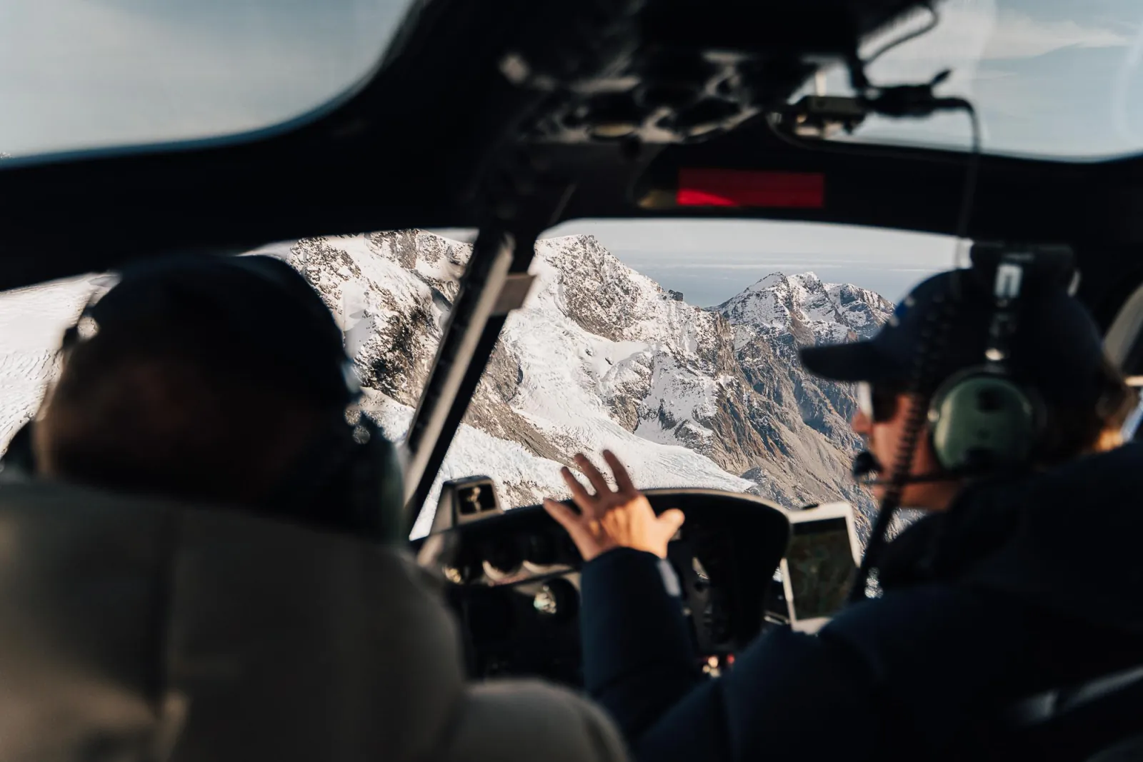 Pilot pointing ahead from the cockpit as the helicopter approaches snowy mountain ridges