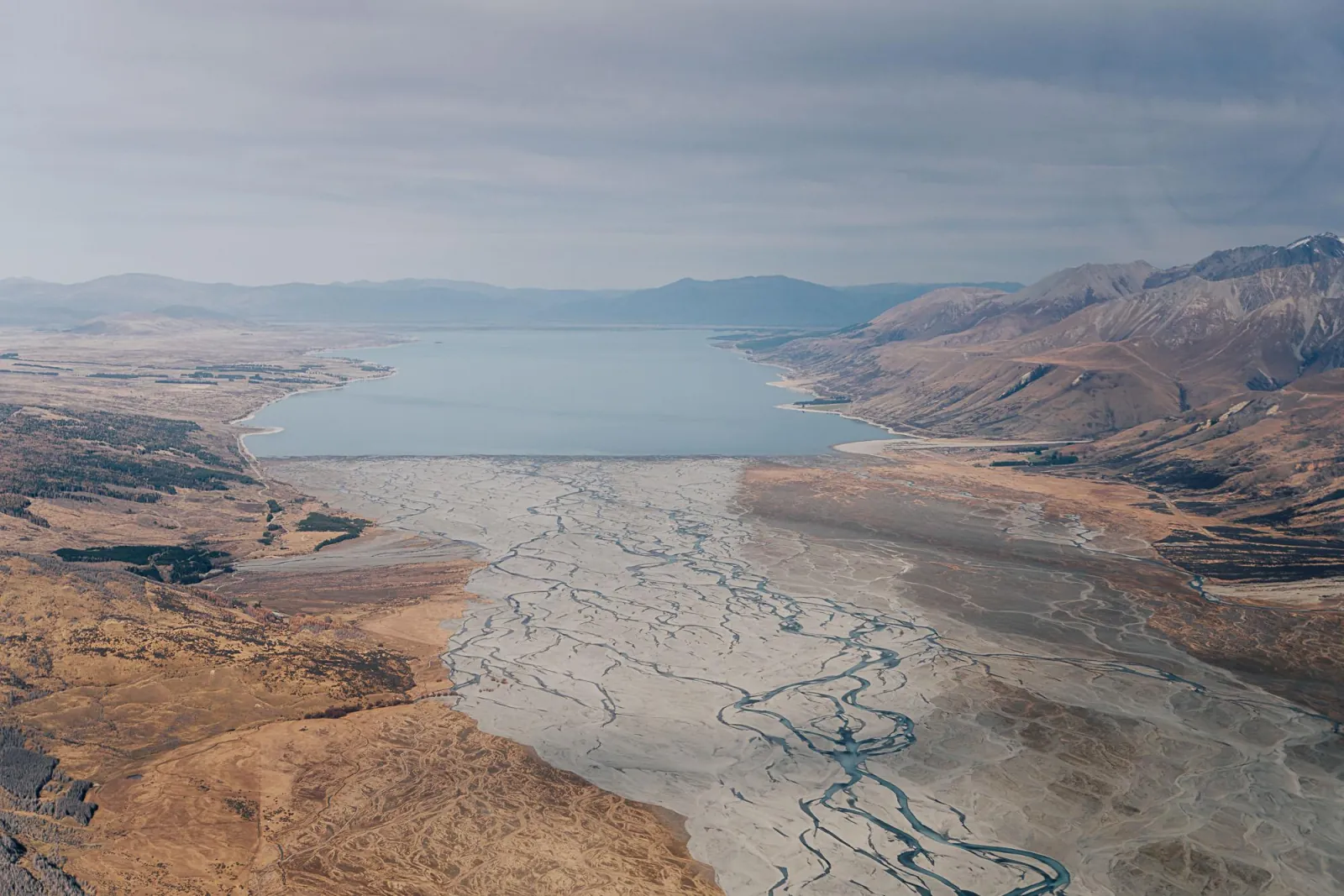 Aerial view of the braided Tasman River flowing into Lake Pūkaki between tussock hills