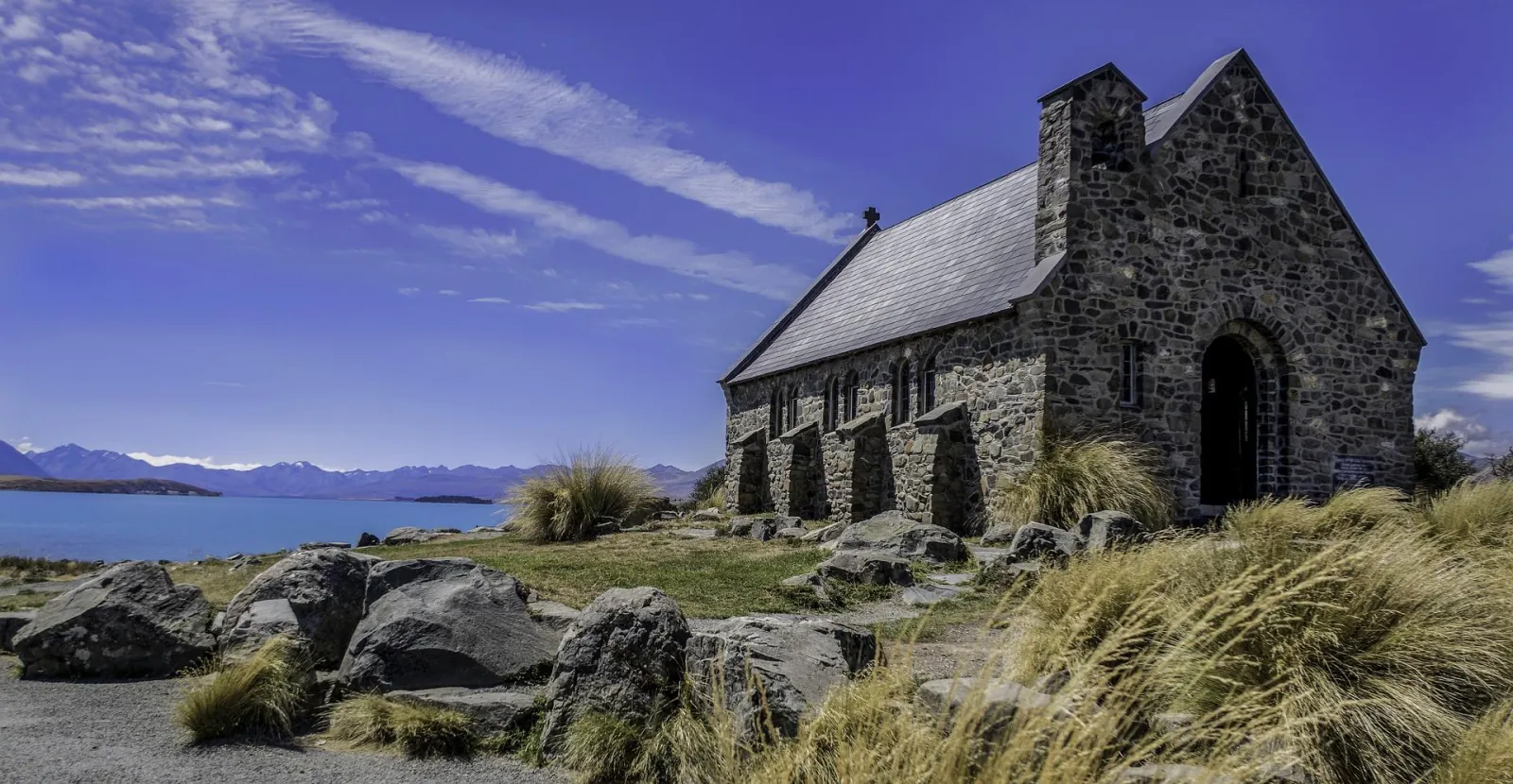 Stone walls of the Church of the Good Shepherd close up, with Lake Tekapo and distant ranges to the left