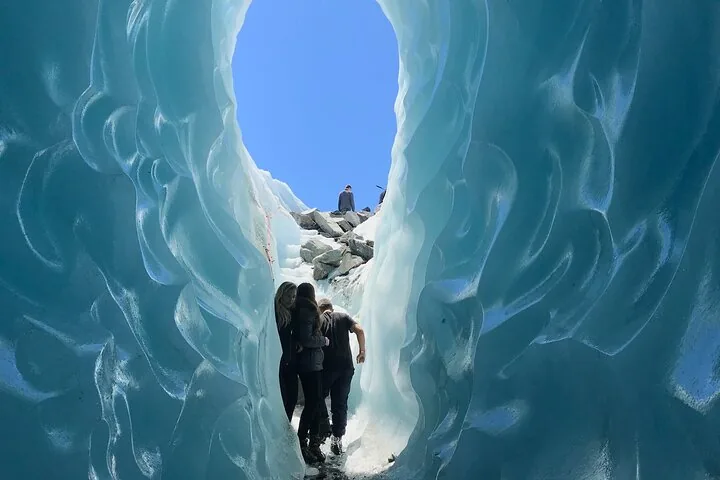Hikers inside a blue ice cave that opens to the sky on the glacier