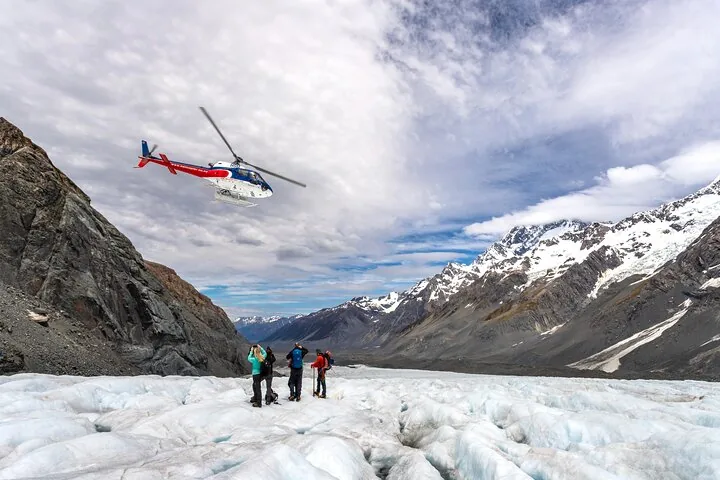 Red and white helicopter flying above a small group of hikers on the glacier ice