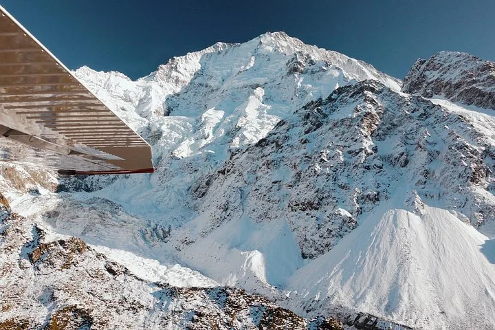 Snow-covered mountain face and icefall seen beneath the wing of a small plane