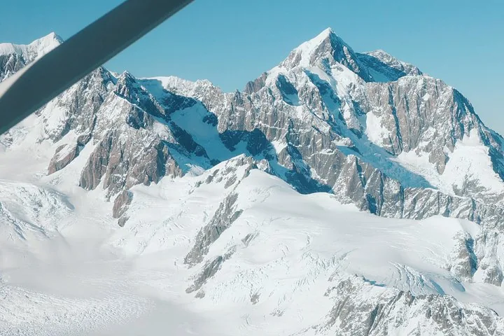 Snow and rock peaks above a glacier, seen past the wing strut of a small plane