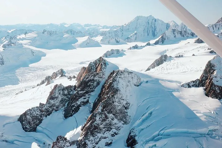 Wide snowfields and rocky peaks of the Southern Alps seen from the window of a small plane