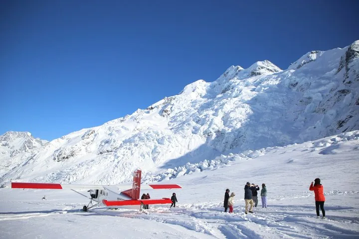 Passengers taking photos beside a ski plane on the glacier, below a wide icefall