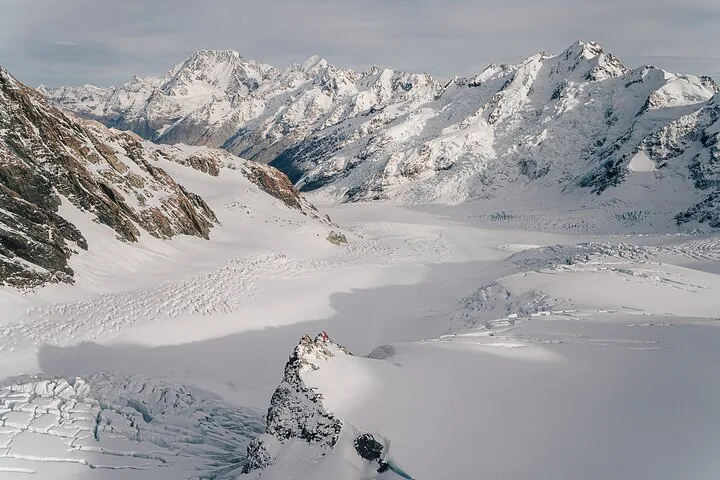 Aerial view over a wide glacier snowfield and crevasses toward a line of snow-covered peaks