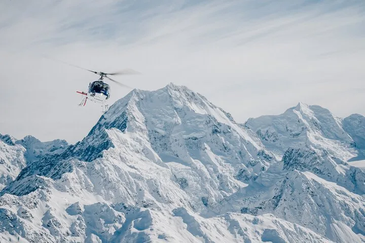 Helicopter flying beside a massive snow-covered peak in Aoraki/Mount Cook National Park