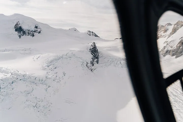 Crevassed glacier ice and dark rock spires seen through a helicopter window