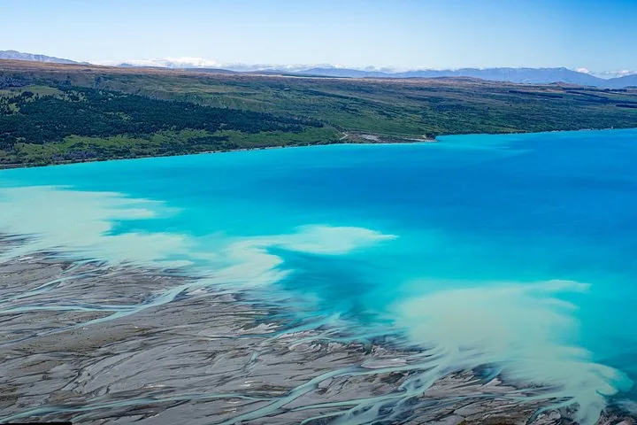 Aerial view of turquoise lake water meeting a grey braided river delta at the head of Lake Pūkaki